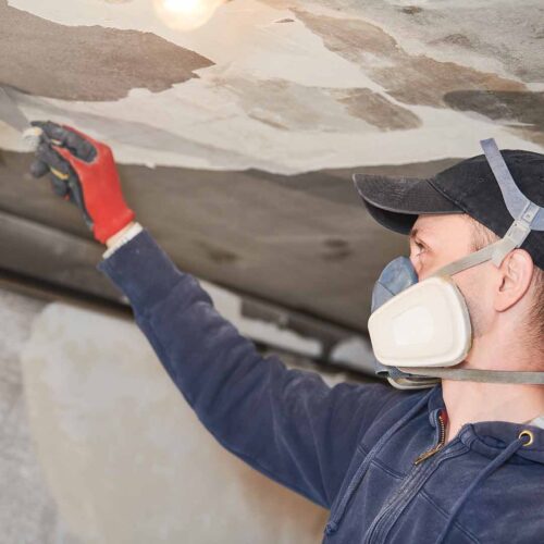 Worker inspecting damaged wall with respirator